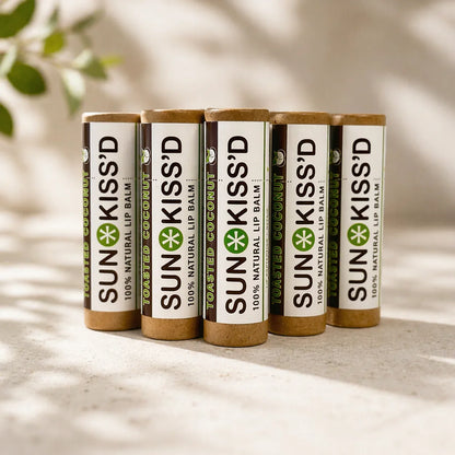 Five Sunkiss'd toasted coconut natural lip balm tubes on a beige surface with soft lighting.