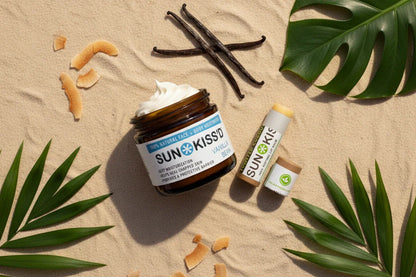 Vanilla bean coconut skincare bundle with moisturizer and lip balm on sand, tropical leaves.